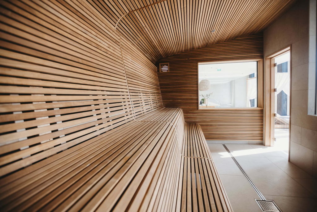 Intérieur de sauna contemporain avec panneaux muraux en bois nervuré, éclairage intégré et disposition des bancs soigneusement étudiée.